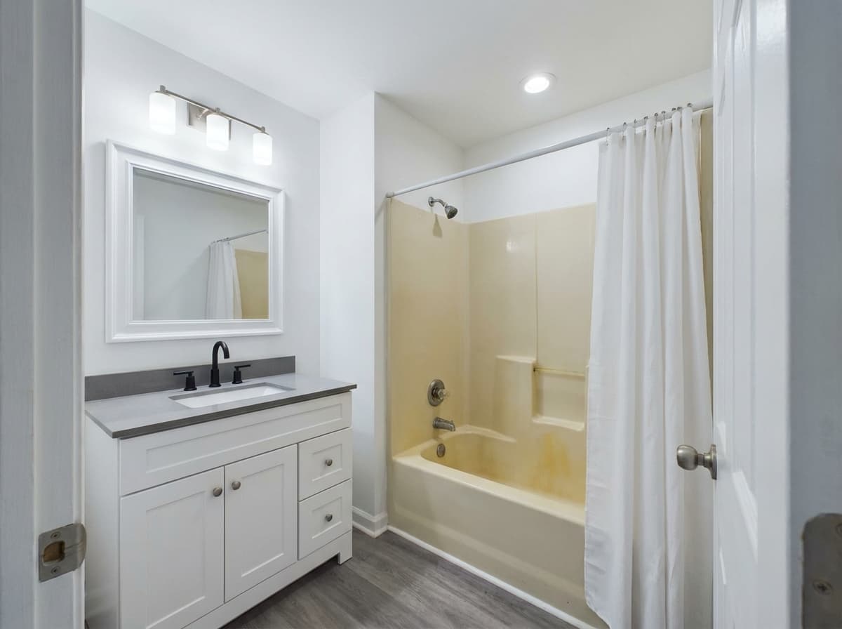 Dated 1990s bathtub and shower combo with yellowed fiberglass, shower curtain, and oak vanity